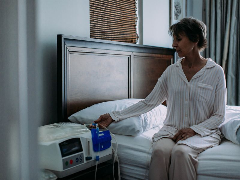 A woman sits on her bed and presses a button on her dialysis machine