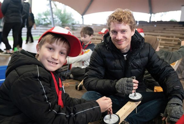 A young student poses with a teacher while they fix a go-kart