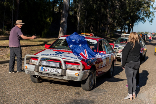 A red Kidney Kar Rally car passes people